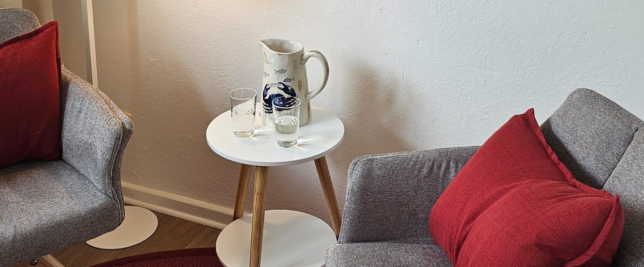 EmpathieundMeer(6) Blick auf die beiden Sesselstühle in der Praxis, dazwischen Beistelltisch mit Wasserkaraffe und zwei Gläser